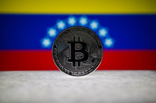 Physical silver version of Bitcoin (BTC) and Venezuela Flag on the background. Conceptual image for investors in cryptocurrency and Blockchain Technology.