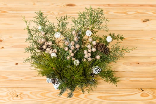 Christmas festive decoration with red baubles, holly with red berries , snow covered pine cones and winter greenery over woodpanel background.