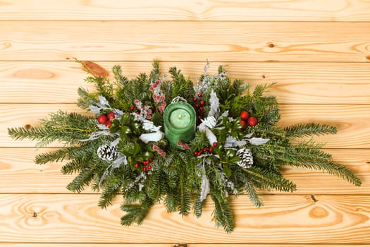 Christmas festive decoration with red baubles, holly with red berries , snow covered pine cones and winter greenery over woodpanel background.