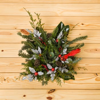 Christmas festive decoration with red baubles, holly with red berries , snow covered pine cones and winter greenery over woodpanel background.