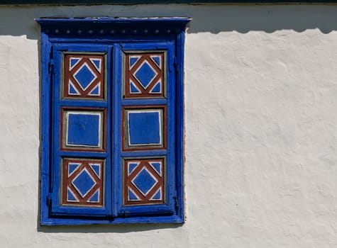 Detail of a traditional village window in Romania painted in strident blue on a white mud wall with copy space.