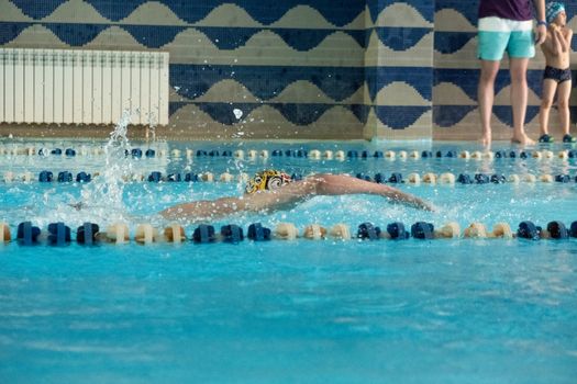 Children swimming freestyle. Indoor swimming pool with clear blue water.