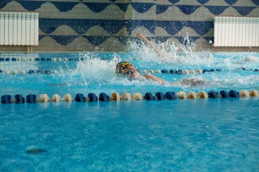 Children swimming freestyle. Indoor swimming pool with clear blue water.