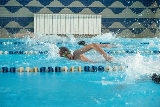 Children swimming freestyle. Indoor swimming pool with clear blue water.