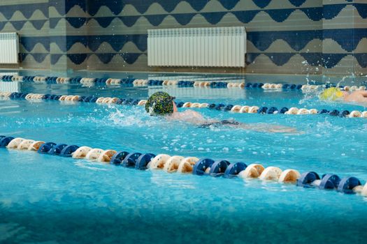 Children swimming freestyle. Indoor swimming pool with clear blue water.