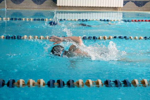 Children swimming freestyle. Indoor swimming pool with clear blue water.