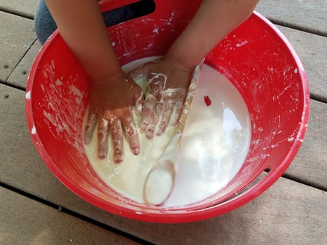 kid with hands playing in red bucket with white slime and wooden spoon on deck