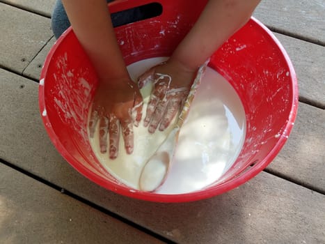 kid with hands playing in red bucket with white slime and wooden spoon on deck