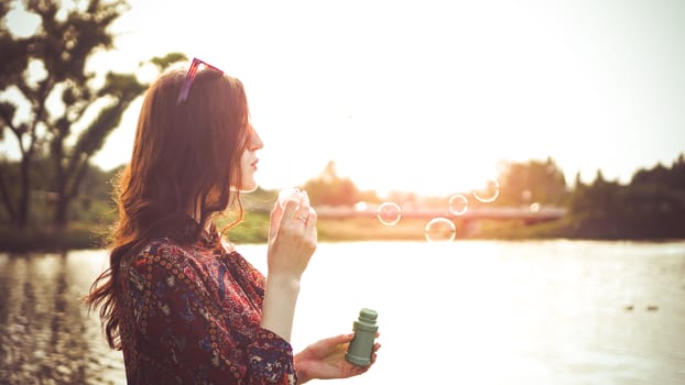 Romantic portrait of young woman with soap balloons. Sunny Valley and river on a summer day