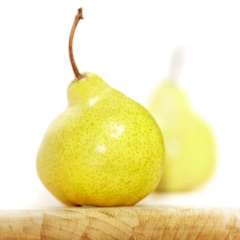 Two naturally crooked pears on a white background with a wooden base. Soft focus view.
