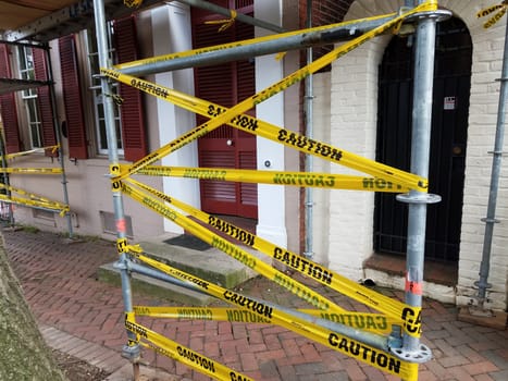 construction scaffolding with yellow warning tape and brick sidewalk