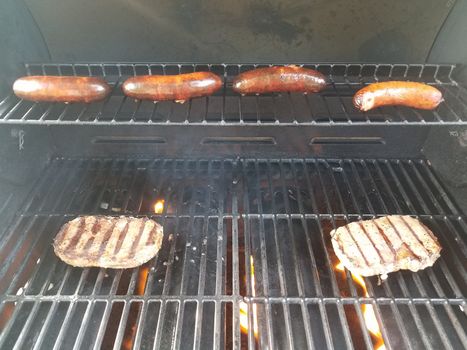 sausages and steaks cooking on hot barbecue grill