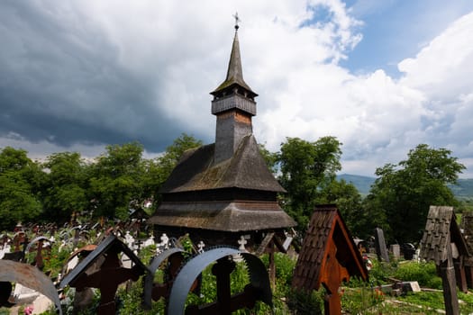 Ieud Hill Church and its graveyard, the oldest wood church in Maramures, Romania under dramatic sky. The Church belongs to a collection of Wooden Churches of Maramures, UNESCO World Heritage Site.