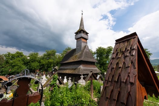 Ieud Hill Church and its graveyard, the oldest wood church in Maramures, Romania under dramatic sky. The Church belongs to a collection of Wooden Churches of Maramures, UNESCO World Heritage Site.