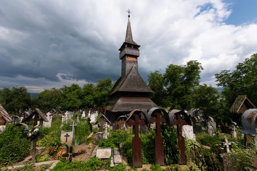 Ieud Hill Church and its graveyard, the oldest wood church in Maramures, Romania under dramatic sky. The Church belongs to a collection of Wooden Churches of Maramures, UNESCO World Heritage Site.