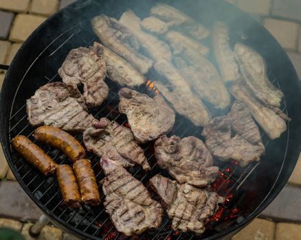 Grilling meats outdoors in a rustic old iron grill an hot coals for family gathering.