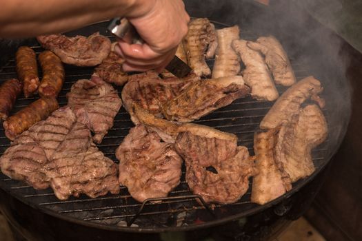 Grilling meats outdoors in a rustic old iron grill an hot coals for family gathering.