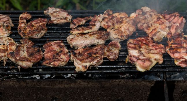 Grilling meats outdoors in a rustic old iron grill an hot coals for family gathering.