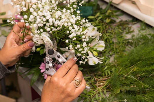 Florist female making a bouquet of different flowers at working table.