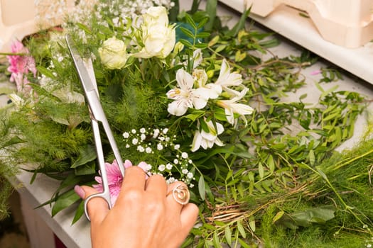 Florist female making a bouquet of different flowers at working table.