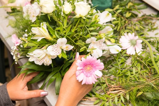 Florist female making a bouquet of different flowers at working table.