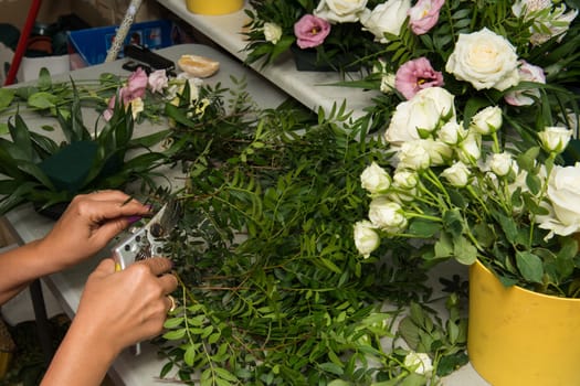 Florist female making a bouquet of different flowers at working table.