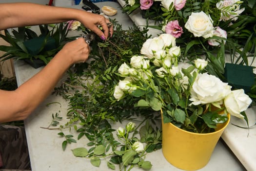 Florist female making a bouquet of different flowers at working table.