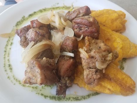 fried pork with onions and bananas with green sauce on plate from Puerto Rico