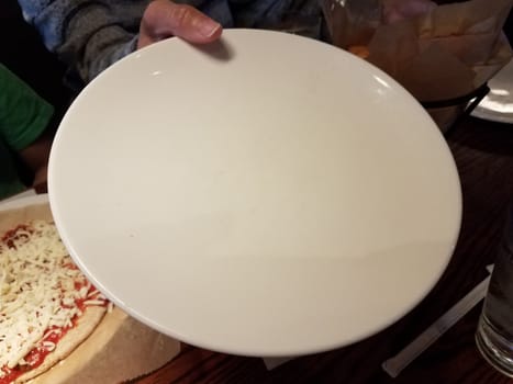 woman's hand holding empty white plate near a cheese pizza