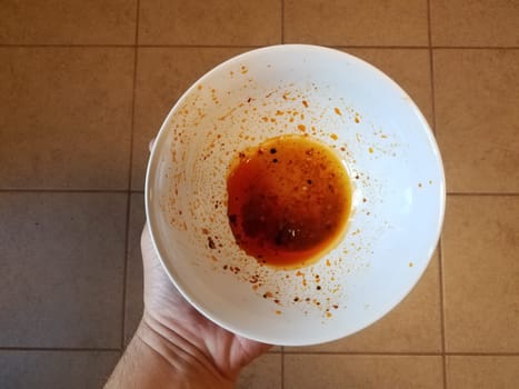 hand holding red oil in white plastic container over tiles