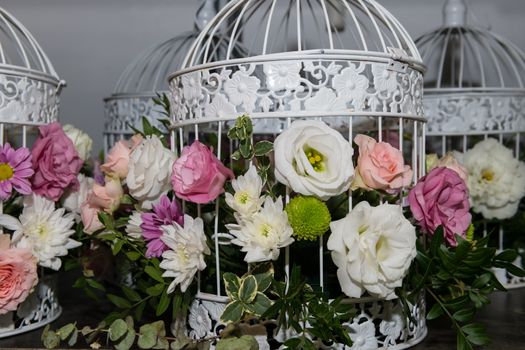 Various bridal flower heads in vintage ornate bird cage as bloom decoration at a wedding reception.