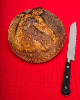 A fresh loaf of round artisan sourdough bread with a breaqd knife.