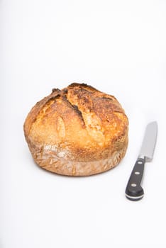 A fresh loaf of round artisan sourdough bread with a breaqd knife.