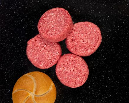 Fresh raw prime black Angus beef burger patties and bread bun on black stone background.