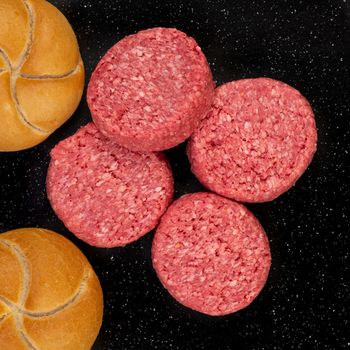 Fresh raw prime black Angus beef burger patties and bread buns on black stone background.