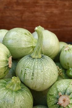 Close up fresh new green baby round zucchini in wooden box on retail display of farmers market, high angle view