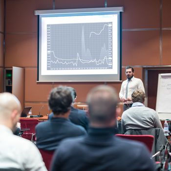 Public Speaker Giving a Talk at Business Meeting. Audience in the conference hall. Skilled coach asks questions to participants of business training. Business and Entrepreneurship concept.