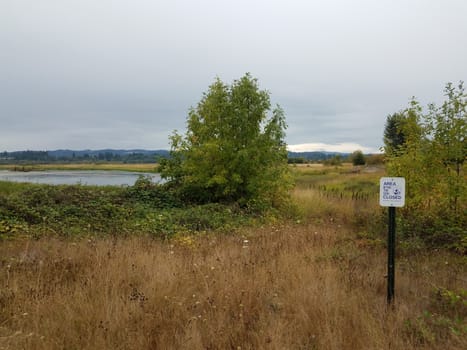 area beyond this sign closed and brown grasses and trees and lake