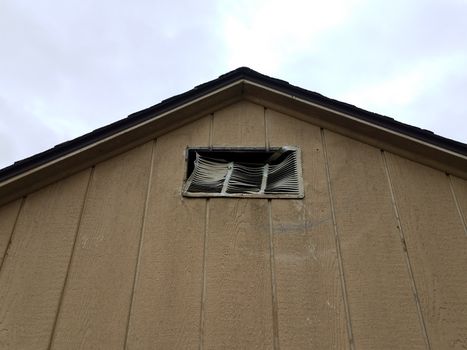 brown storage shed building with damaged or broken metal vent