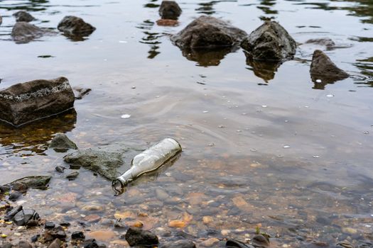 A clear bottle lies in the river as litter polluting the environment.