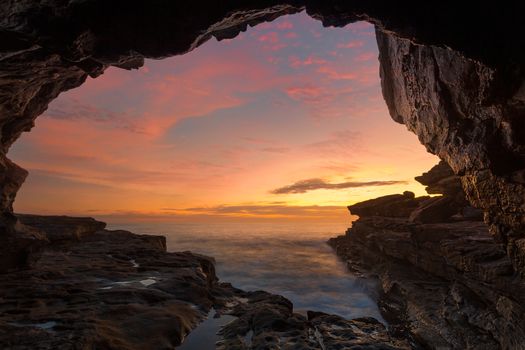 Cave views frame a view to a spectacular ocean sunrise of yellpws reds amd b;ies