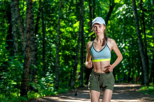 portrait of a beautiful muscular sportswoman while jogging in a summer park