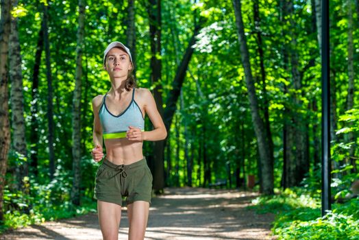 horizontal portrait of an active beautiful muscular sportswoman while jogging in a summer park