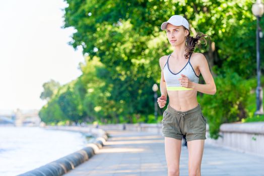 portrait of a running sports woman on the embankment in a city park in sportswear