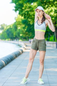 girl with a muscular figure is warming up on the city embankment before jogging