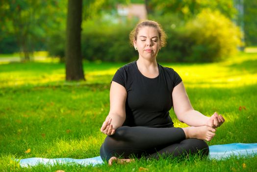 concentrated woman oversize meditates on the lawn in the park in the lotus position