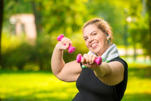 portrait of smiling plus size woman with dumbbells in the park during workout