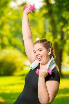 Satisfied plump woman doing her exercise in the park, exercise with dumbbells