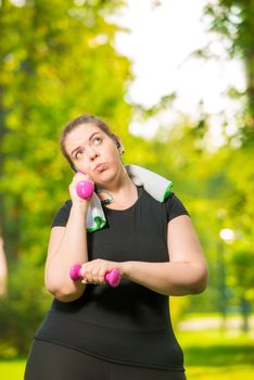 Portrait of a pensive plus size model engaged with dumbbells during a workout in a summer park