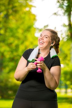 happy woman 30 years old plus size without complexes deals with dumbbells during a workout in a summer park